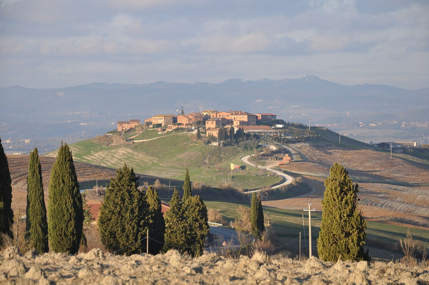 Le colline argillose delle crete senesi a Mucigliani, con cipressi e un borgo sul crinale